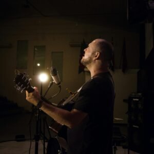 A musician passionately playing guitar and singing on a dimly lit stage.